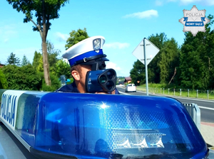 policjant z laserowym miernikiem prędkości, obok niebieska lampa na dachu radiowozu z napisem POLICJA - poziom