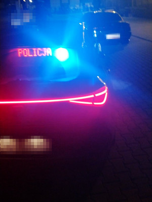 noc, tył nieoznakowanego radiowozu, na wyświetlaczu napis POLICJA, w tle zatrzymany do kontroli pojazd