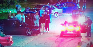 policjant przy nieoznakowanym radiowozie, obok samochody i młode osoby