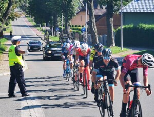 1. Umundurowany policjant ruchu drogowego, kieruje uchem,  w tle peleton (2)