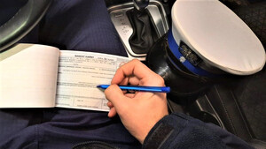 wnętrze radiowozu, policjant wypełnia bloczek mandatowy, obok policyjna czapka