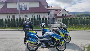 Policjant WRD obok dwa  policyjne motocykle w tle budynek szkoły