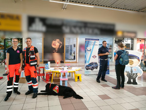 policjant rozmawia z kobietą i jej dzieckiem, obok ratownicy medyczni i pies służbowy