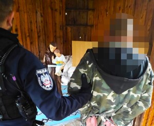 policjant przytrzymuje podejrzewanego który na nadgarstkach ma założone kajdanki
