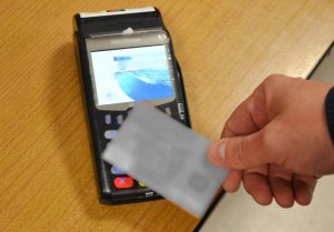 płatność zbliżeniowa - dłoń zbliżająca kartę bankomatową do terminala płatniczego