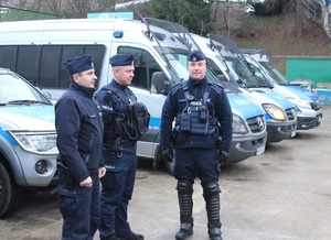 Umundurowani policjanci podczas zabezpieczenia w tle radiowozy oznakowane