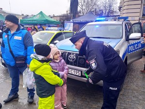 policjant wręcza dzieciom elementy odblaskowe